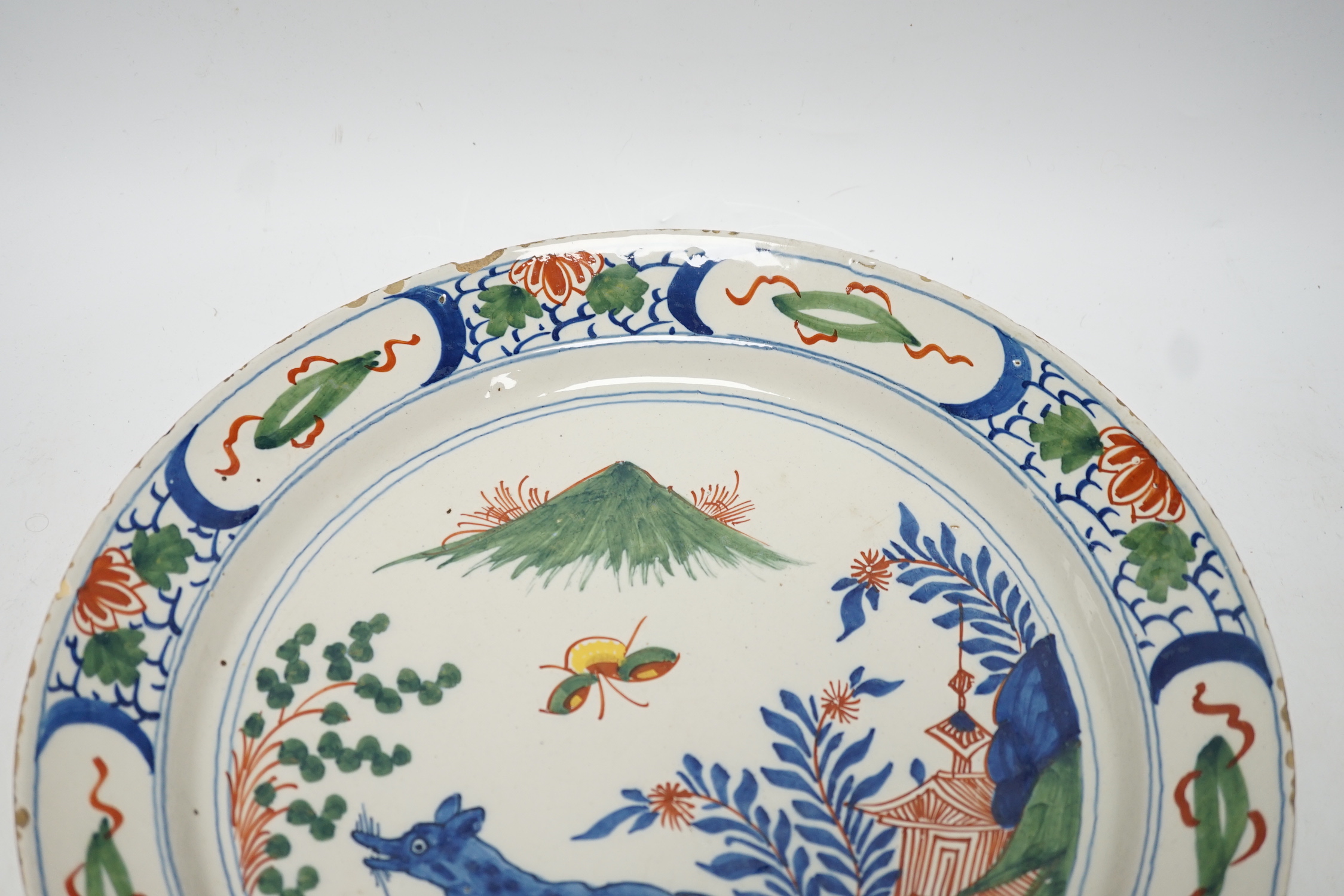 An 18th century Delft dish, the centre painted with a wolf, a bee and a pavilion, 35cm